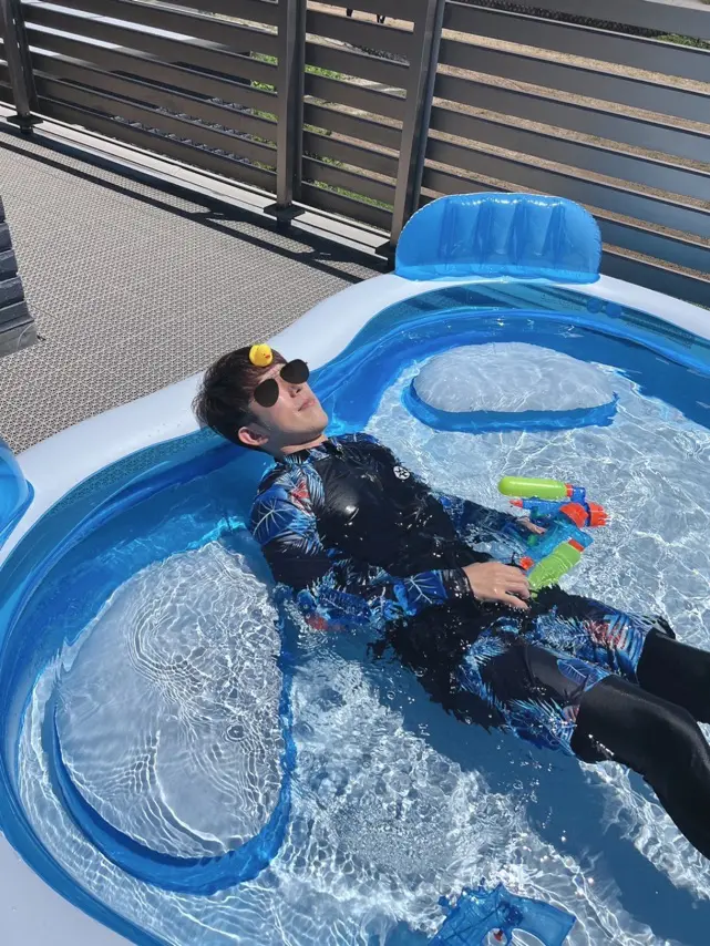 男性が水鉄砲を手にビニールプールに浮かんでいる